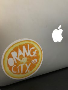 Orange City, IA sticker in the shape of an orange on Jacquelyn's MacBook, showing her pride for being from Orange City, Iowa. 