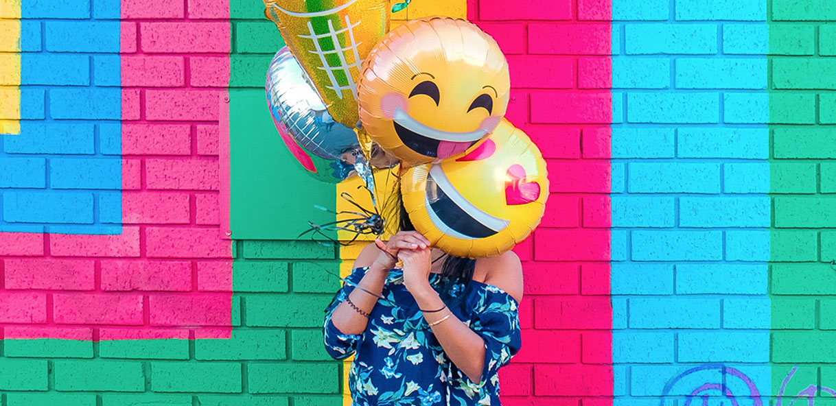 Woman holding emoji balloons against a colorful background.
