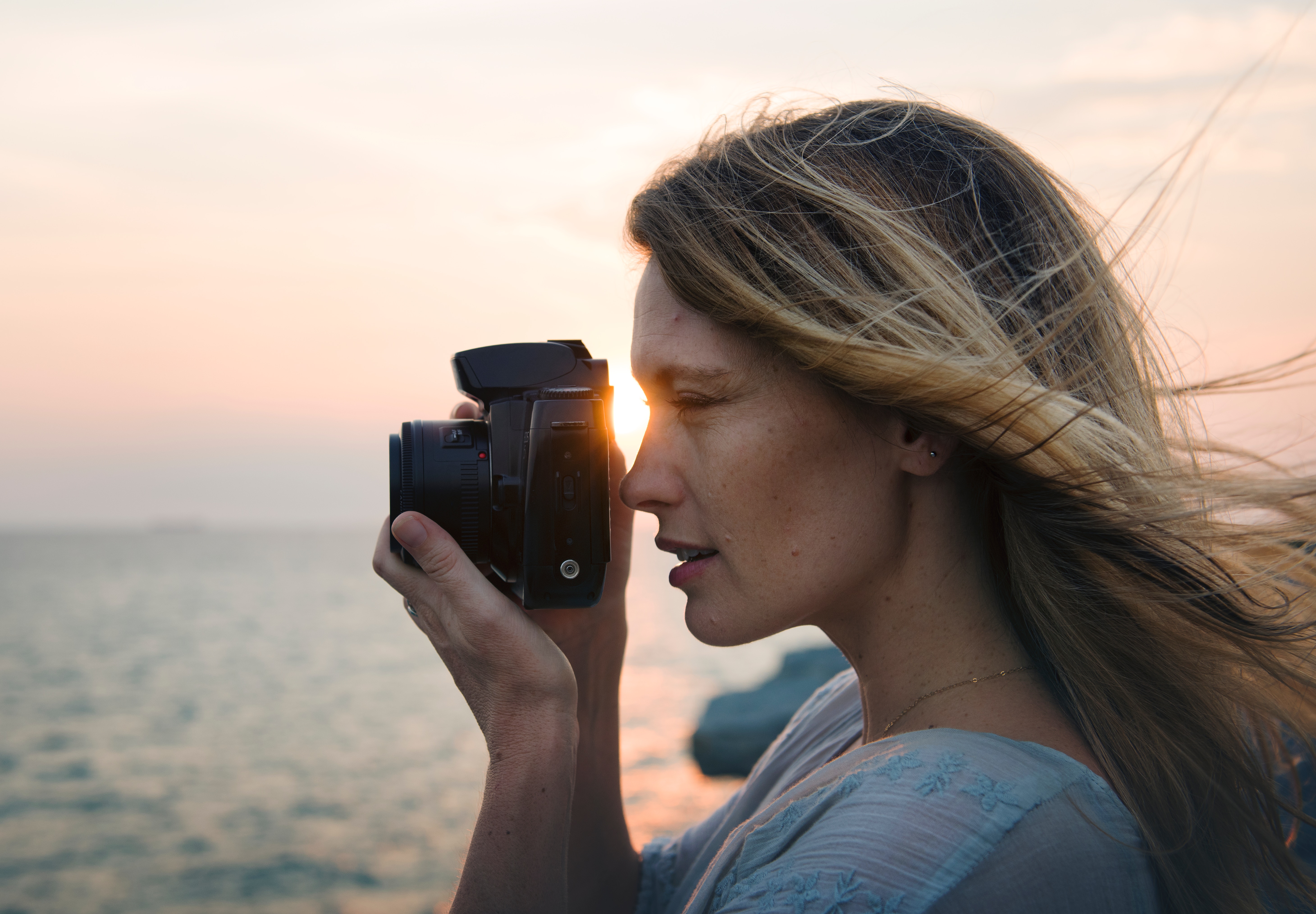 Woman taking photograph with sunset and ocean behind her