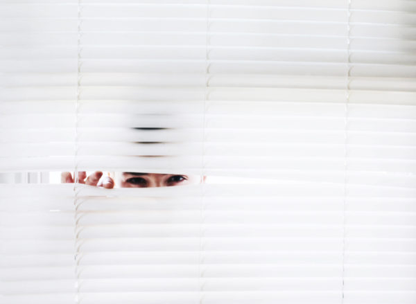 Man peeking from behind white blinds because he is tentative of being a data marketer