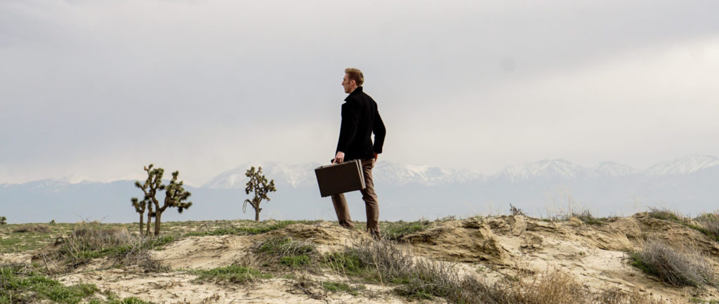 a man standing in the middle of a prairie holding a briefcase