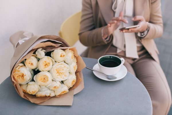bouquet of white roses beside cup of tea and person holding a phone