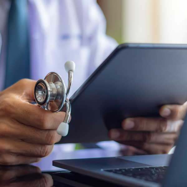 closeup of doctor holding tablet in front of laptop
