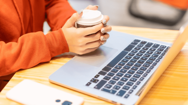 Person holding a coffee cup over their open laptop.